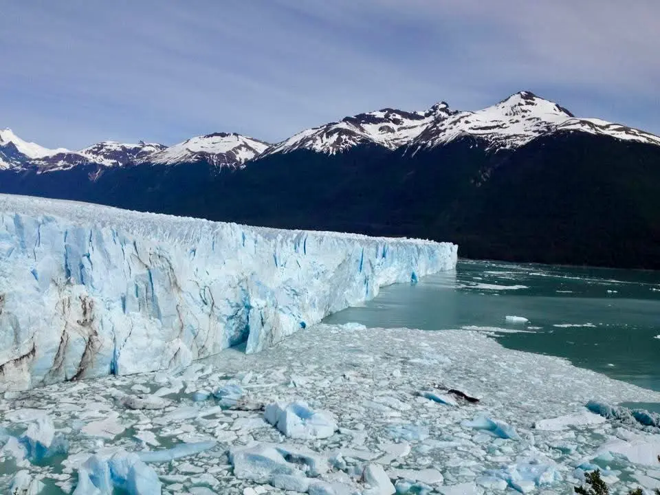 Expansive glacier meeting icy water with snow-capped mountains in the background.